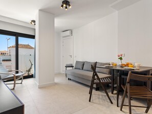 A modern living room with a sofa, dining table, and chairs, a balcony with a view, and an air conditioning unit. - La Joya 1B. New apartment in Carihuela, 300 m from the beach (Torremolinos)