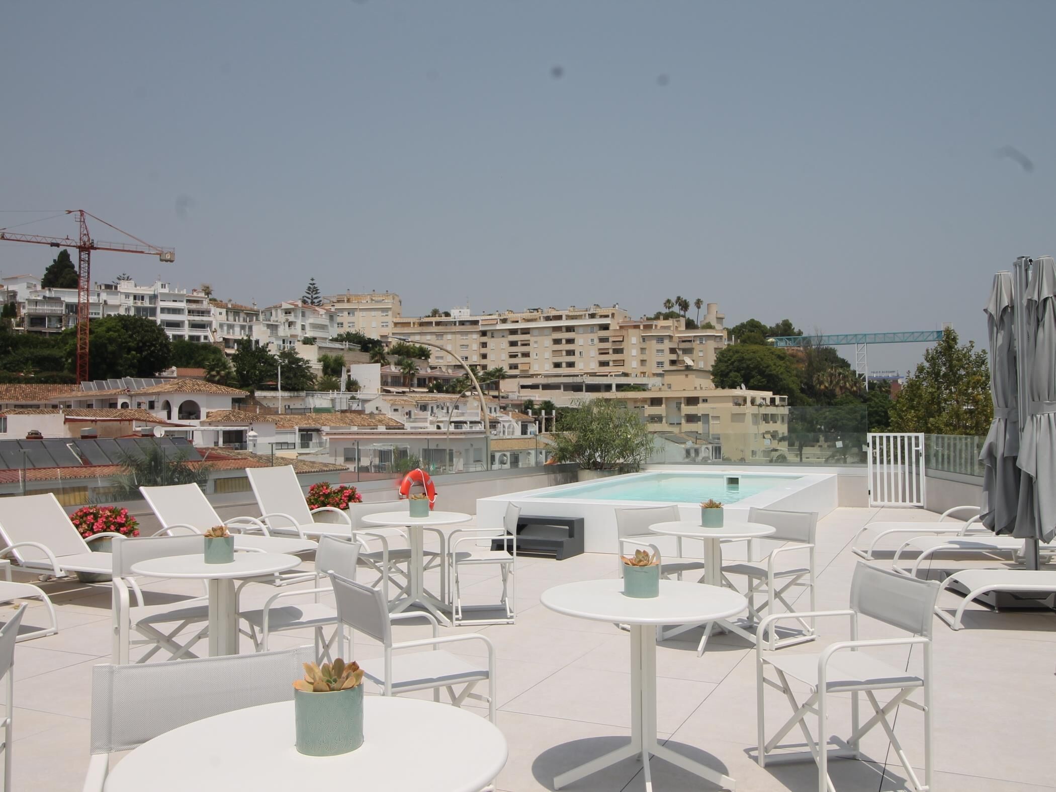 Una terrazza sul tetto con poltrone e tavoli, una piscina e vista sulla città, con edifici e un ponte.