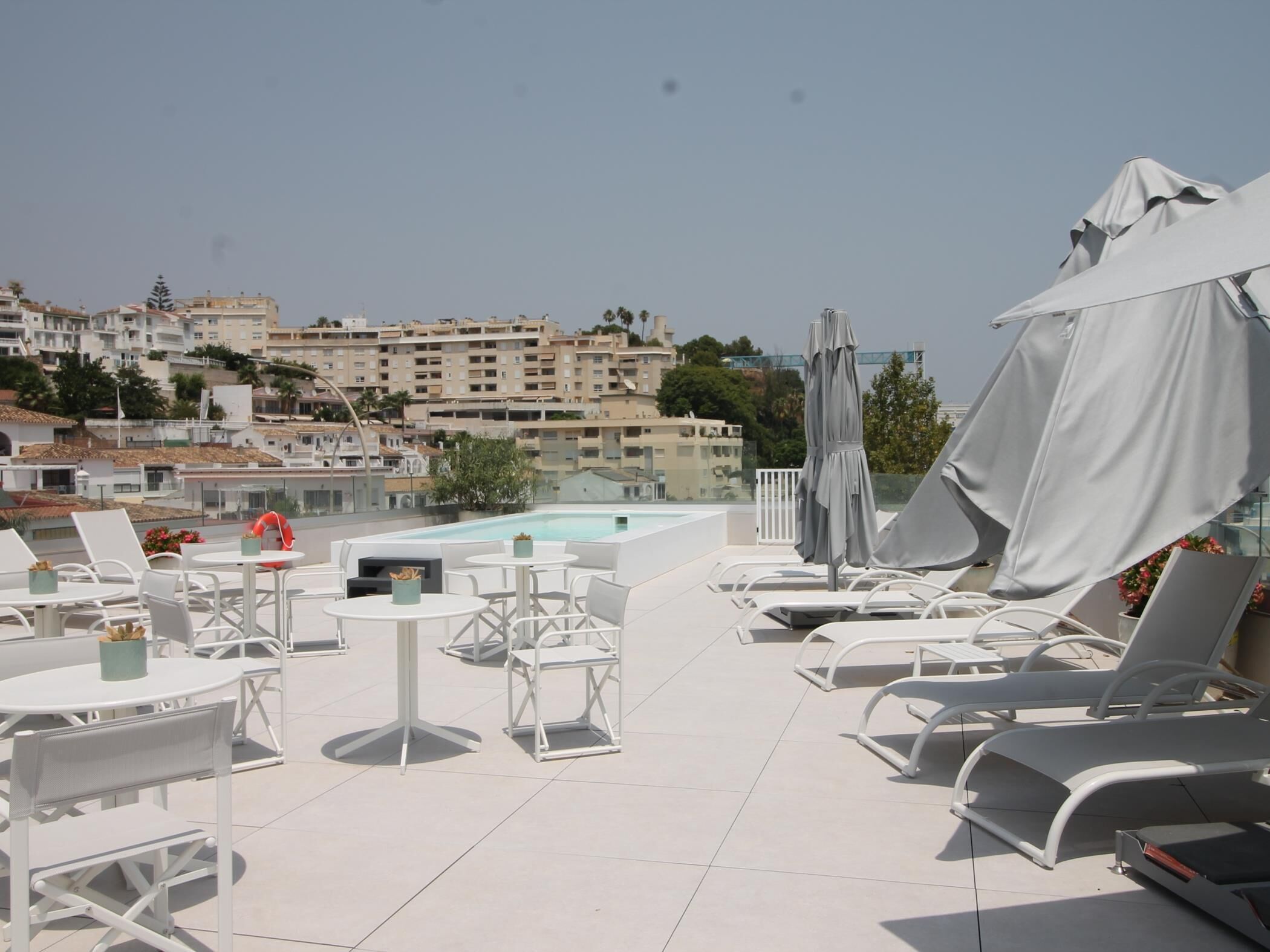 Terraço no telhado com piscina, cadeiras de lounge brancas e guarda-sóis.