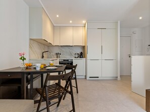 A modern kitchen with white cabinets, a marble backsplash, and a dining area with a dark wooden table and chairs. - La Joya 1B. New apartment in Carihuela, 300 m from the beach (Torremolinos)