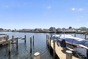 A waterfront dock with a covered boat, wooden pilings, and a row of houses in the background.