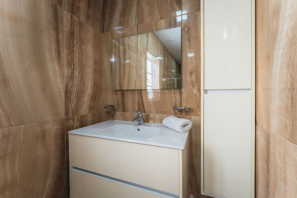 Une salle de bain avec un mur en marbre, un lavabo avec un miroir et une serviette.