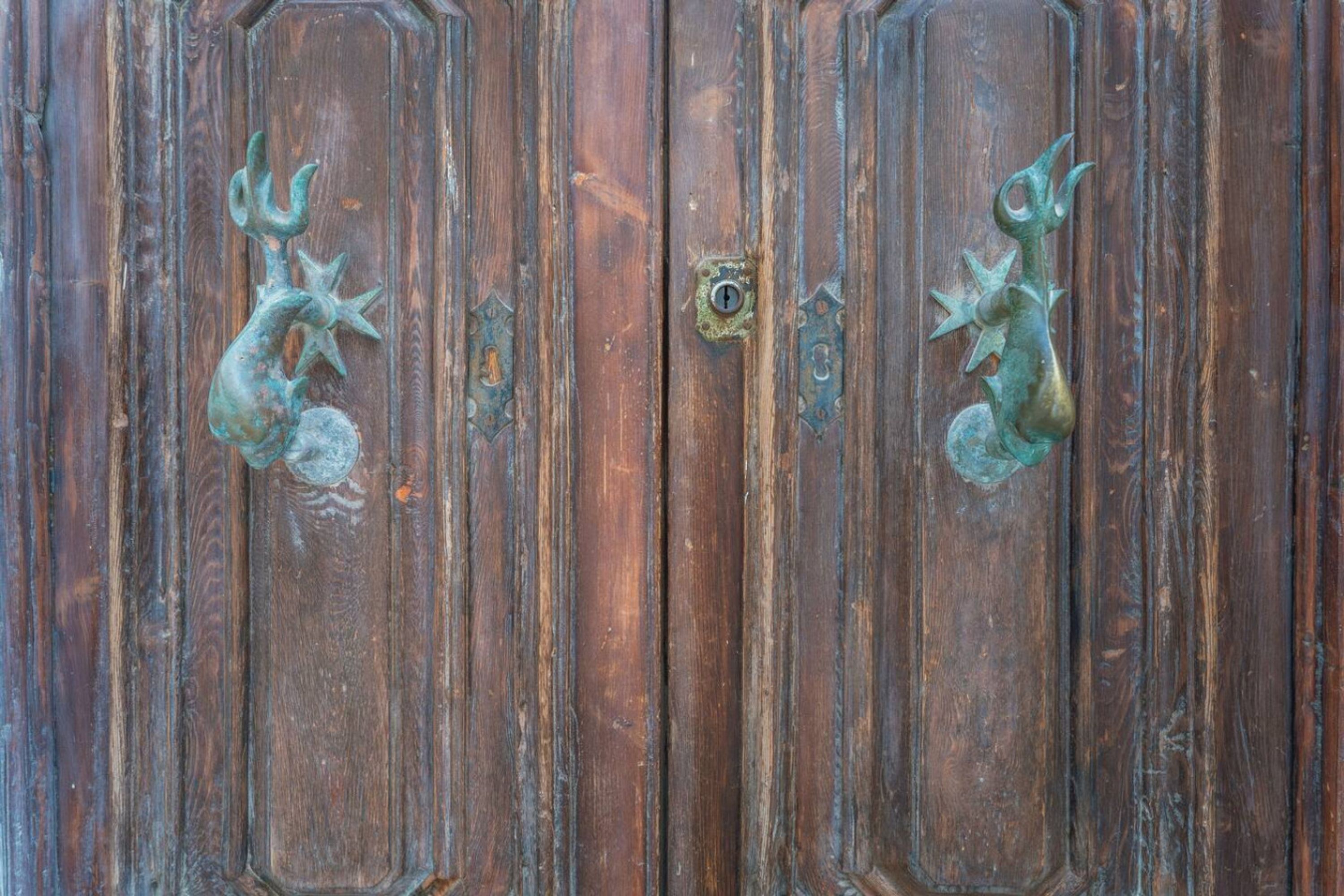 Puerta de madera con dos manijas metálicas y un cerrojo central.