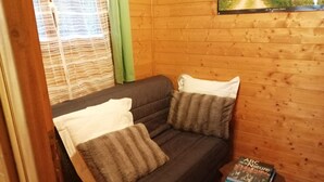 Una habitación acogedora con un sofá de color oscuro, dos almohadas, una pequeña mesa con un libro y paredes de madera.