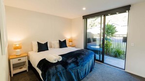 A bedroom with a bed, two bedside tables with lamps, a sliding glass door to a balcony, and a view of the outdoors. - Beach Nearby | Balcony | Stroll to Town – KK77018 (Kaikōura)