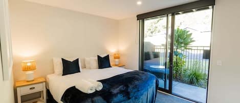 A bedroom with a bed, two bedside tables with lamps, a sliding glass door to a balcony, and a view of the outdoors.