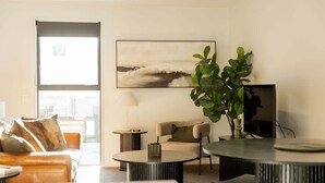 A modern living room with a sofa, a round coffee table, a lamp, and a large plant. - Beach Nearby | Balcony | Stroll to Town – KK77018 (Kaikōura)