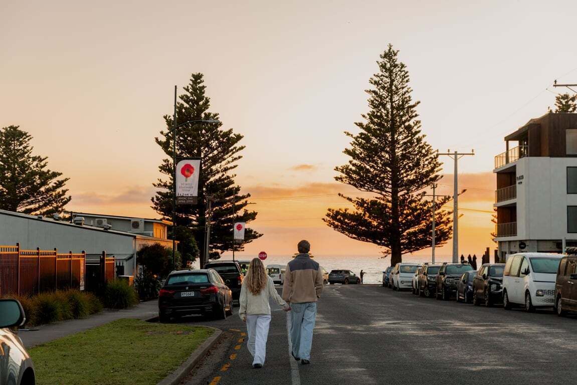 A street with parked cars, a couple walking, and buildings with balconies.