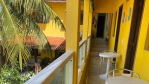 Un couloir aux murs jaunes, une balustrade en verre et des tables blanches avec des chaises en métal.
