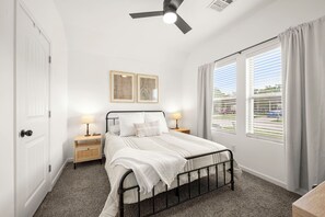 Une chambre à coucher avec un lit, deux lampes de chevet, un ventilateur de plafond, une fenêtre avec des rideaux et une porte.