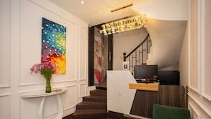 A modern reception area with a marble counter, a staircase, and a colorful abstract painting. - Luma Boutique Hotel (Hanoi)