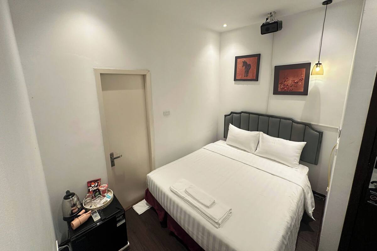 Een hotelkamer met een bed, een nachtkastje met een waterkoker, een dienblad met snacks en een deur.