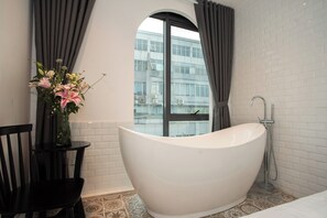 Une salle de bain moderne avec une baignoire sur pieds, une fenêtre avec des rideaux et un vase rempli de fleurs posé sur une table.