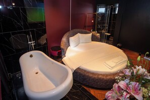 Une salle de bain moderne avec une baignoire, un lit rond doté d’une tête de lit moelleuse et un petit tabouret rouge.