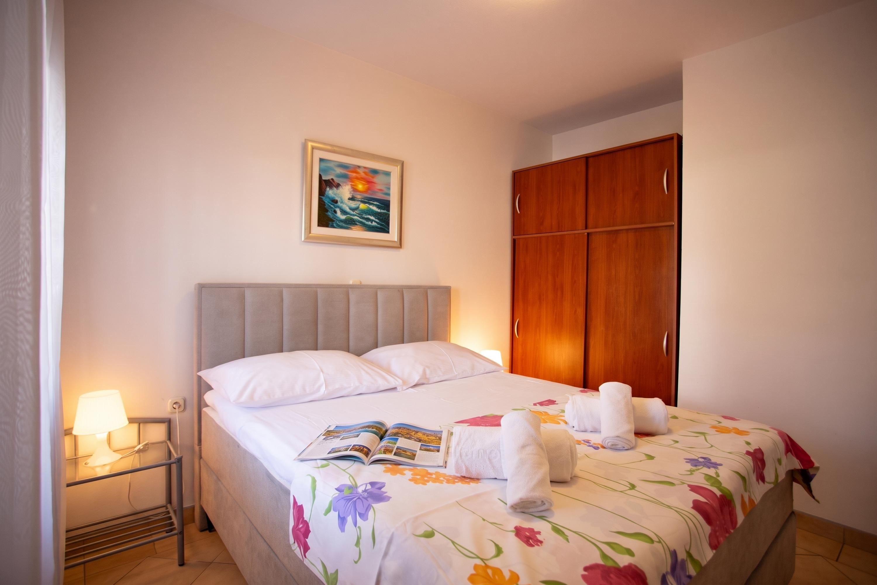 Ein Hotelzimmer mit Bett, Nachttisch, Lampe, Kleiderschrank und einem Gemälde an der Wand.