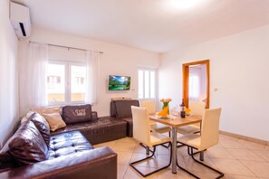 A living room with a brown leather sofa, a dining table with chairs, a flat-screen TV mounted on the wall, and a window with curtains. - Lovely Apartment Vrsar 6 With Balcony, Vrsar, Croatia (Vrsar)