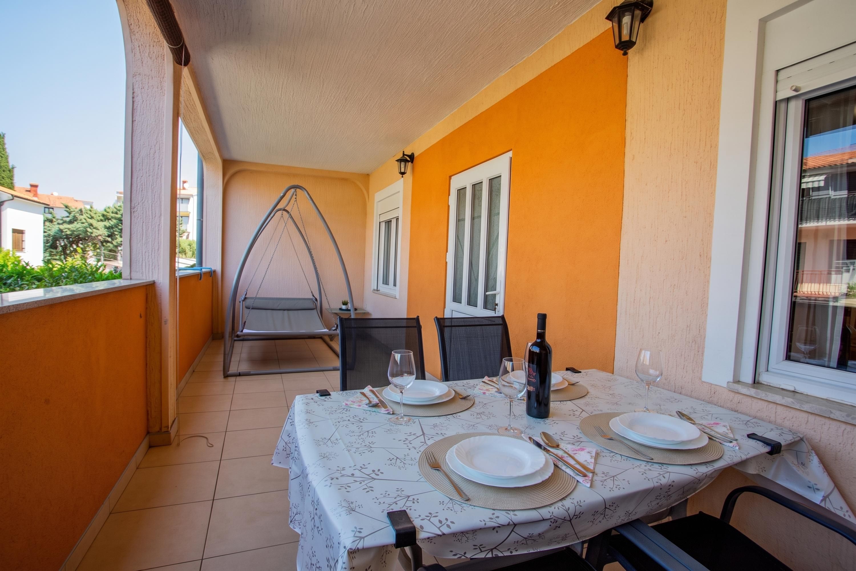 A dining area with a table set for two, a hanging chair, and a bottle of wine.