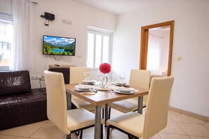 A dining area with a table set for four, a television mounted on the wall, and a window with curtains. - Lovely Apartment Vrsar 6 With Balcony, Vrsar, Croatia (Vrsar)