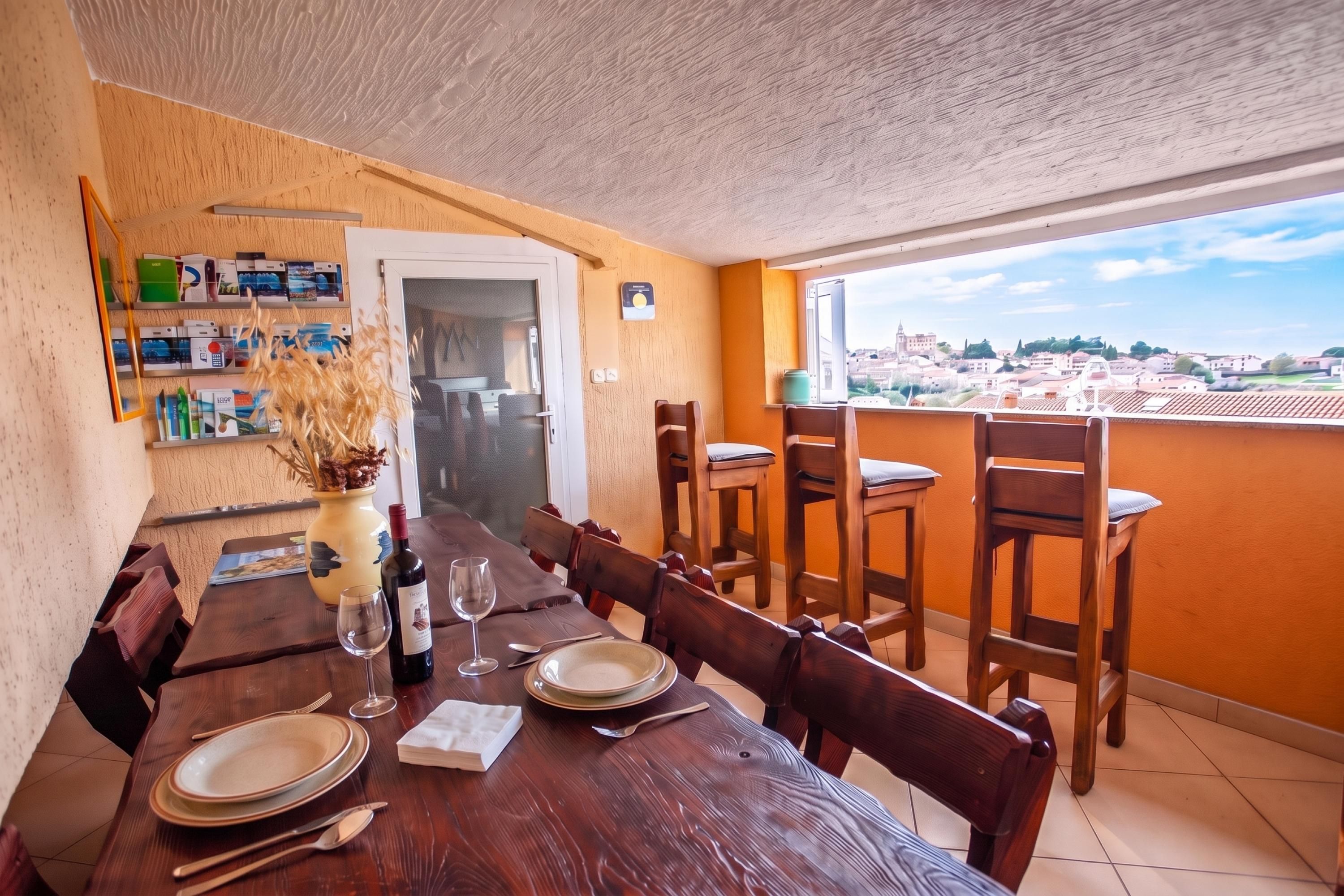 A dining area with a wooden table set for two, a vase with dried flowers, and a bottle of wine.