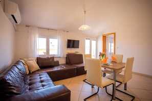 A living room with a brown leather sofa, a dining table with chairs, a flat-screen TV, and a ceiling light fixture. - Lovely Apartment Vrsar 2 With Balcony, Vrsar, Croatia (Vrsar)