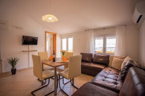 Un salon avec un canapé en cuir marron, une table à manger avec des chaises, un téléviseur fixé au mur et une fenêtre avec des rideaux.