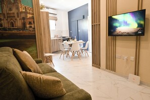 A modern living room with a green sofa, a dining area with a white table and chairs, and a TV displaying the Northern Lights. - Well Located Modern Apart Balluta Bay, St Julian's, Malta (St Julian's)