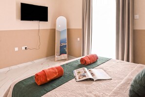 A hotel room with a bed, a flat-screen TV mounted on the wall, a mirror, and a window with curtains. - Walk to Balluta & Spinola - modern 2bdr apart, St Julian's, Malta (St Julian's)