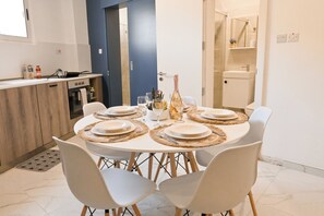 A dining area with a round table set for six, a kitchen in the background, and a bathroom visible through an open door. - Well Located Modern Apart Balluta Bay, St Julian's, Malta (St Julian's)