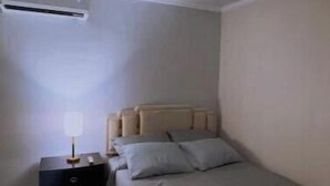 Une chambre à coucher comprenant un lit, une table de chevet, une lampe et un appareil de climatisation.