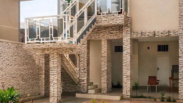 Ein modernes Haus mit Naturstein-Fassade, einer Treppe zu einem Balkon und einem gepflegten Rasen.