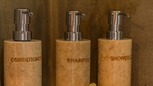 Three cylindrical bottles with pumps, labeled 'CONDITIONER,' 'SHAMPOO,' and 'SHOWER BATH,' arranged on a metal rack. - D'junas Villas (Ubud)