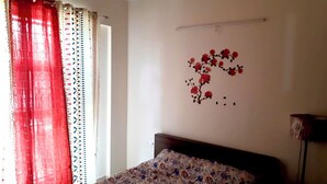 A bedroom with a bed, a wall-mounted shelf, a window with curtains, and a wall decoration. - Enjoyable 3-bedroom apartment with AC in vibrant Bengaluru (Bengaluru)