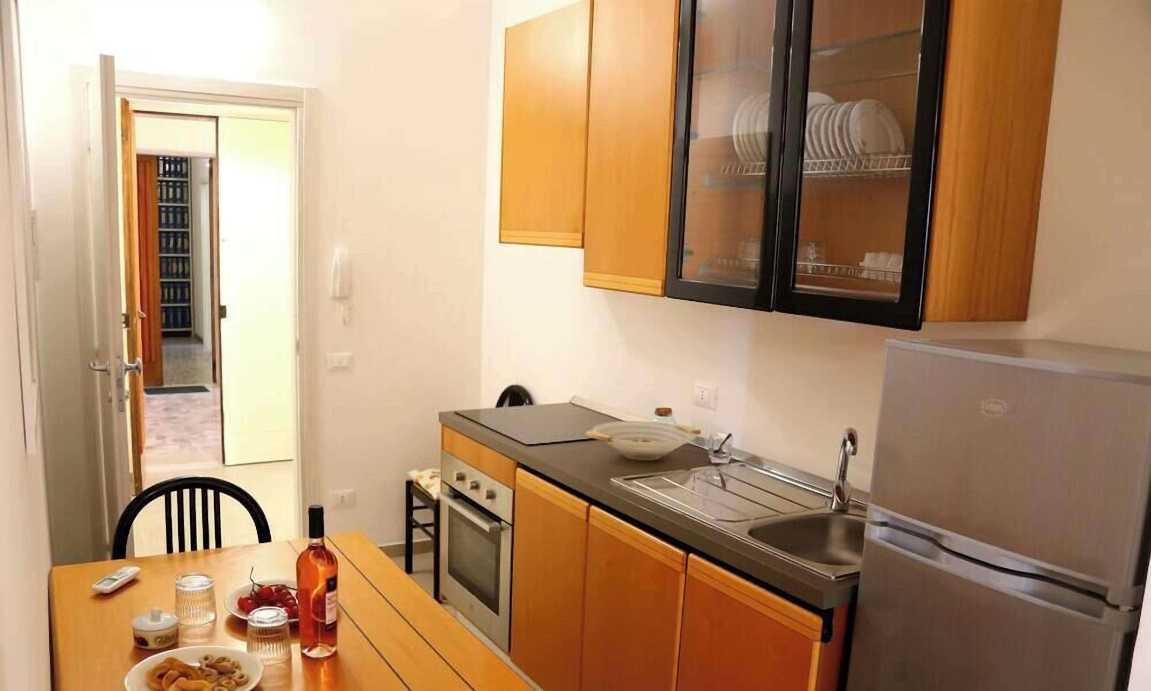 A compact kitchen with wooden cabinets, a stainless steel refrigerator, and a dining table with chairs.