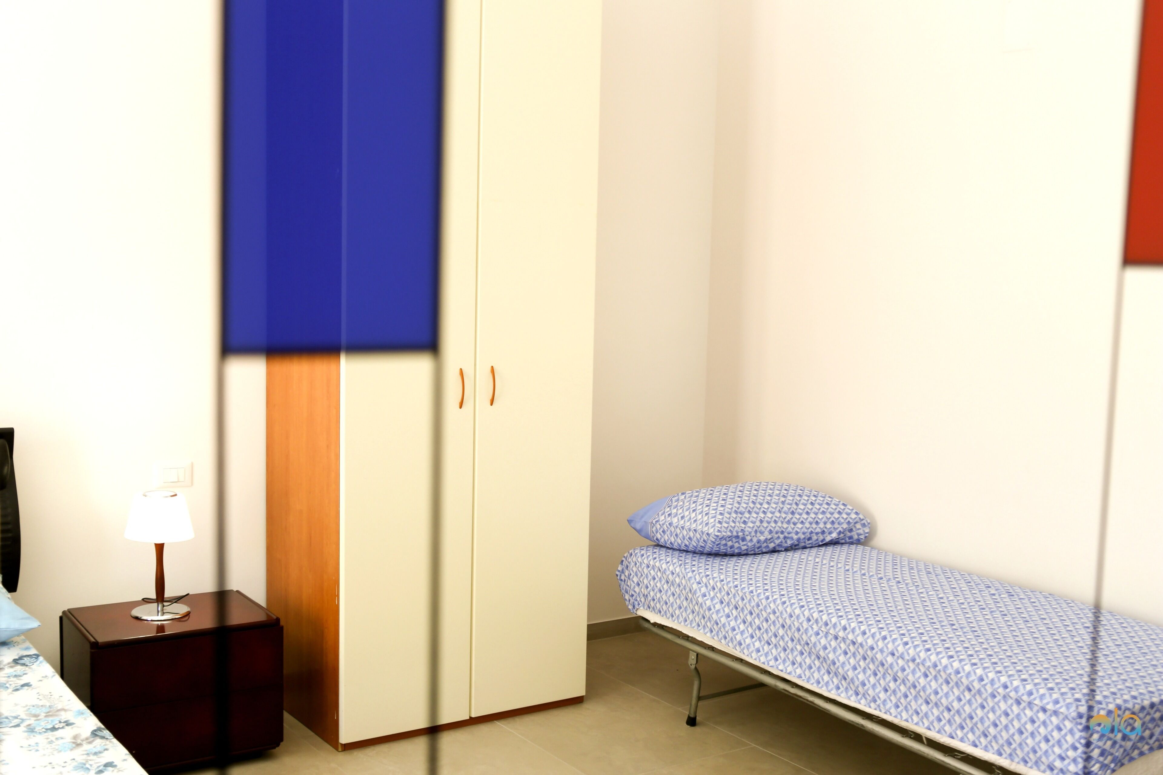 A room with a bed, a wardrobe, and a nightstand with a lamp.
