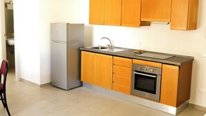 Una cocina compacta con armarios de madera, un refrigerador de acero inoxidable, un lavamanos y un horno.