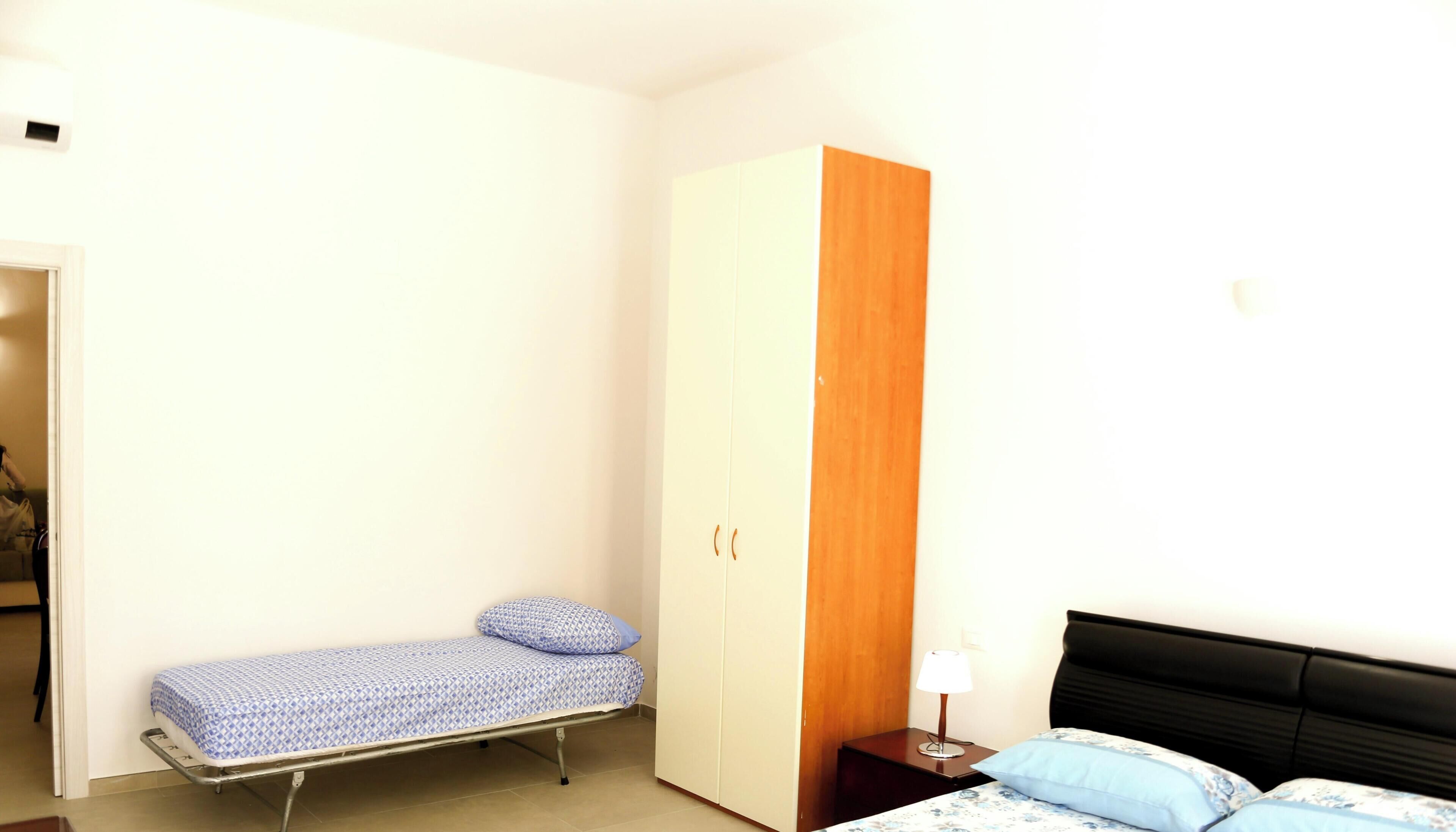Een slaapkamer met een enkel bed, een kledingkast, een nachtkastje en een lamp.