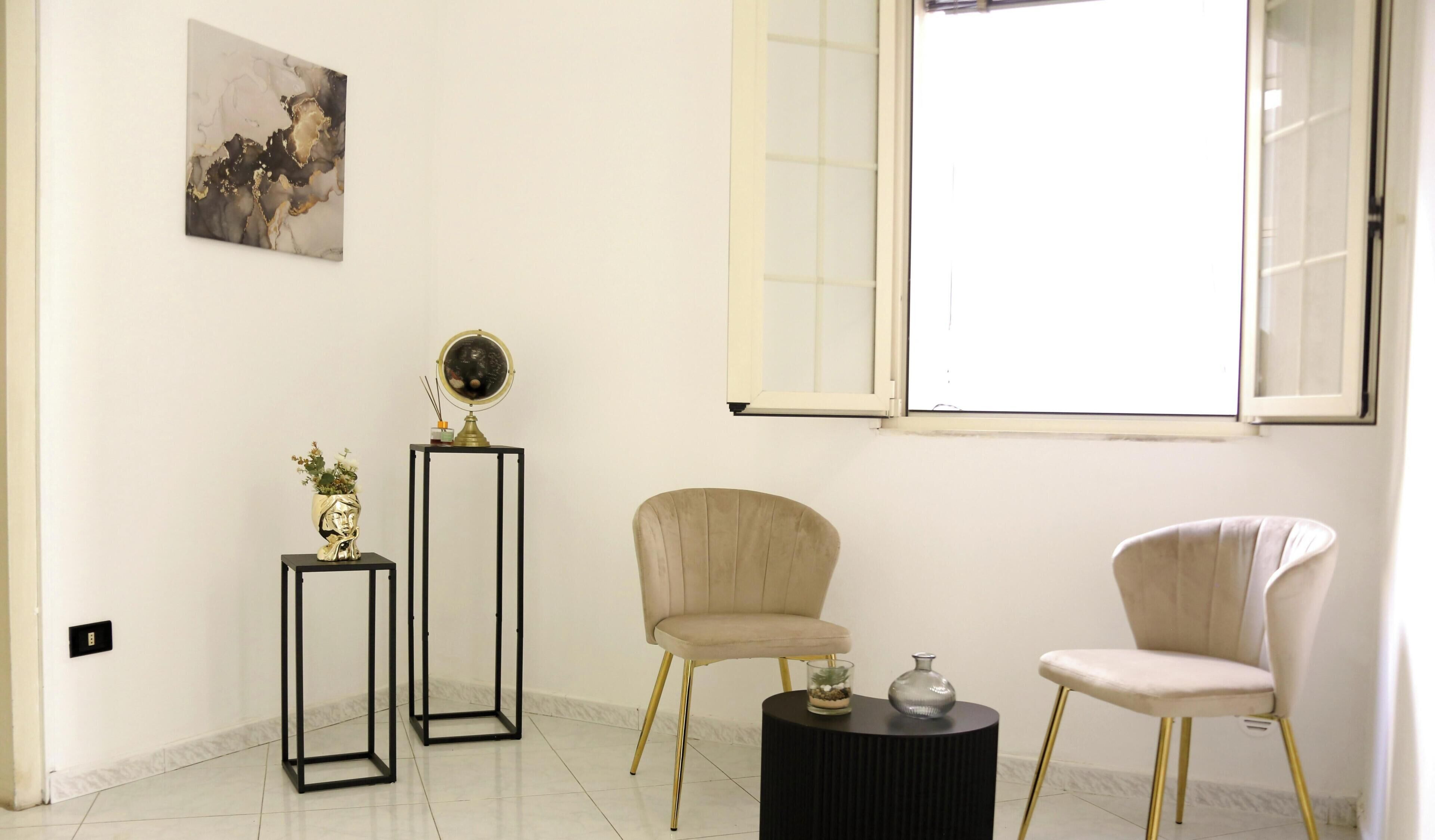 A room with a large window, two chairs, a small table, a globe on a stand, and a painting on the wall.