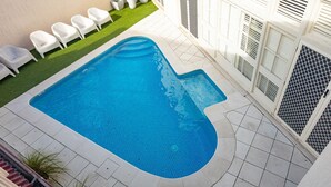 A swimming pool with a tiled deck, surrounded by white chairs and a building with white shutters. - No 11 The Smugglers Inn (Victor Harbor)