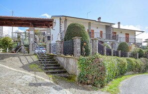 Une maison à deux étages avec un escalier en pierre, une entrée fermée par un portail et un jardin bien entretenu.