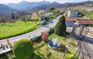 Eine ländliche Straße mit Häusern, einem Brunnen und Bergen im Hintergrund.