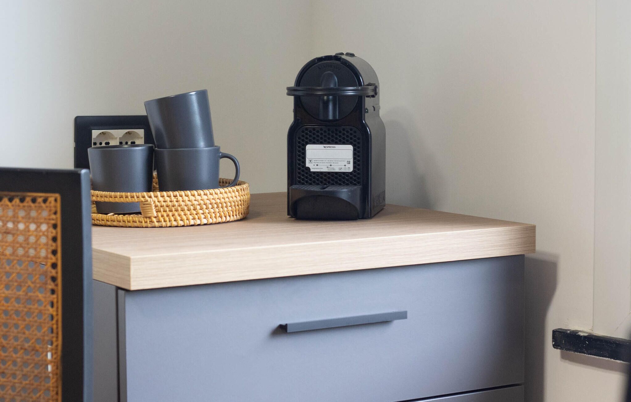 En köksbänk med en kaffebryggare, en korg med koppar och en låda.