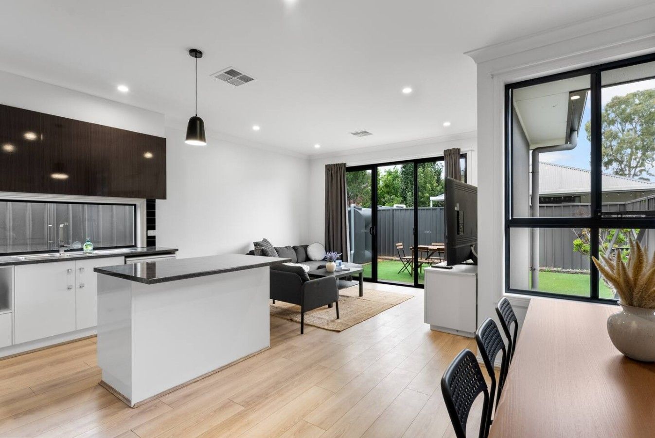 A modern kitchen with a central island, a dining area with a table and chairs, and a large sliding glass door leading to a backyard.
