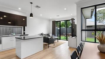 A modern kitchen with a central island, a dining area with a table and chairs, and a large sliding glass door leading to a backyard.