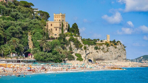 Un hotel sul lungomare con struttura simile a un castello, una spiaggia e un cielo azzurro intenso.
