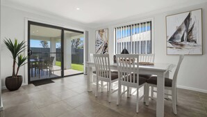 A dining area with a glass door leading to a patio, white chairs, and a sailboat painting on the wall. - Whistling Way Wonderscape - Modern 4 Bed, 2 Bath (Orange)