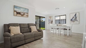 A living room with a sofa, a dining table with chairs, and artwork on the walls. - Whistling Way Wonderscape - Modern 4 Bed, 2 Bath (Orange)
