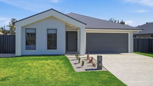A modern single-story house with a garage, a covered driveway, and a well-maintained lawn. - Whistling Way Wonderscape - Modern 4 Bed, 2 Bath (Orange)