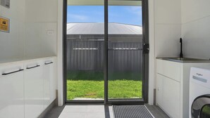 A modern kitchen with a dishwasher, a double door leading to a backyard, and a warning sign on the wall. - Whistling Way Wonderscape - Modern 4 Bed, 2 Bath (Orange)