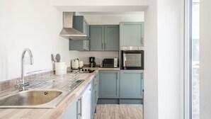 Una cocina moderna con un lavamanos de acero inoxidable, microondas, cafetera y armarios azul claro.