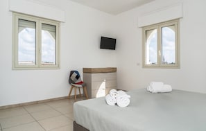 Ein Schlafzimmer mit einem Bett, einem Sessel, einem Fernseher und einem Fenster.